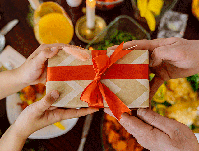 Image of one person handing a wrapped gift to another.