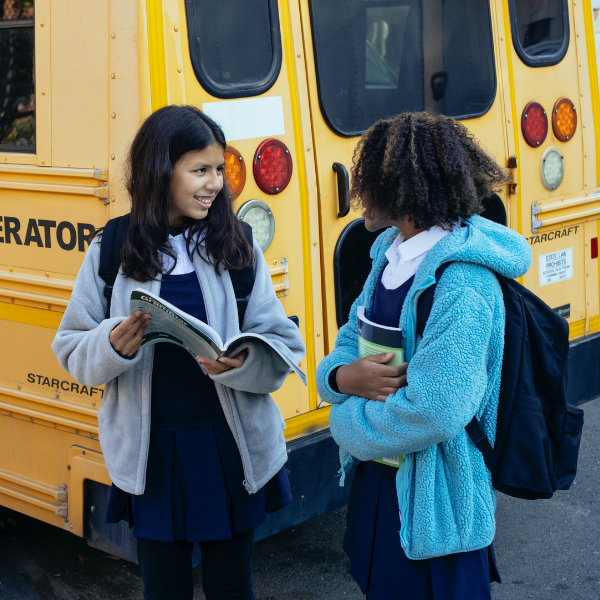 two girls with backpacks in front of a school bus