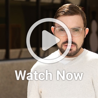 image of man with glasses in front of buidling with a play overlay button