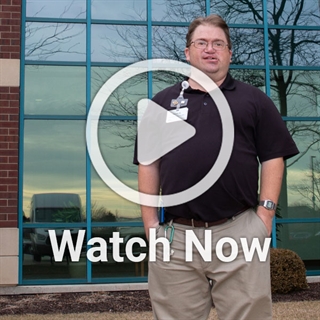 image of man standing in front of building with a play overlay button