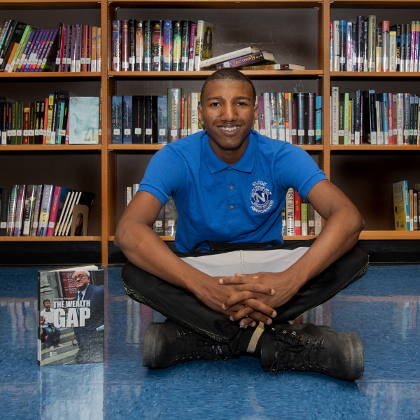 Maleak sitting on the floor with bookshelves behind him.