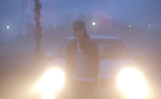 Woman standing in front of car headlights